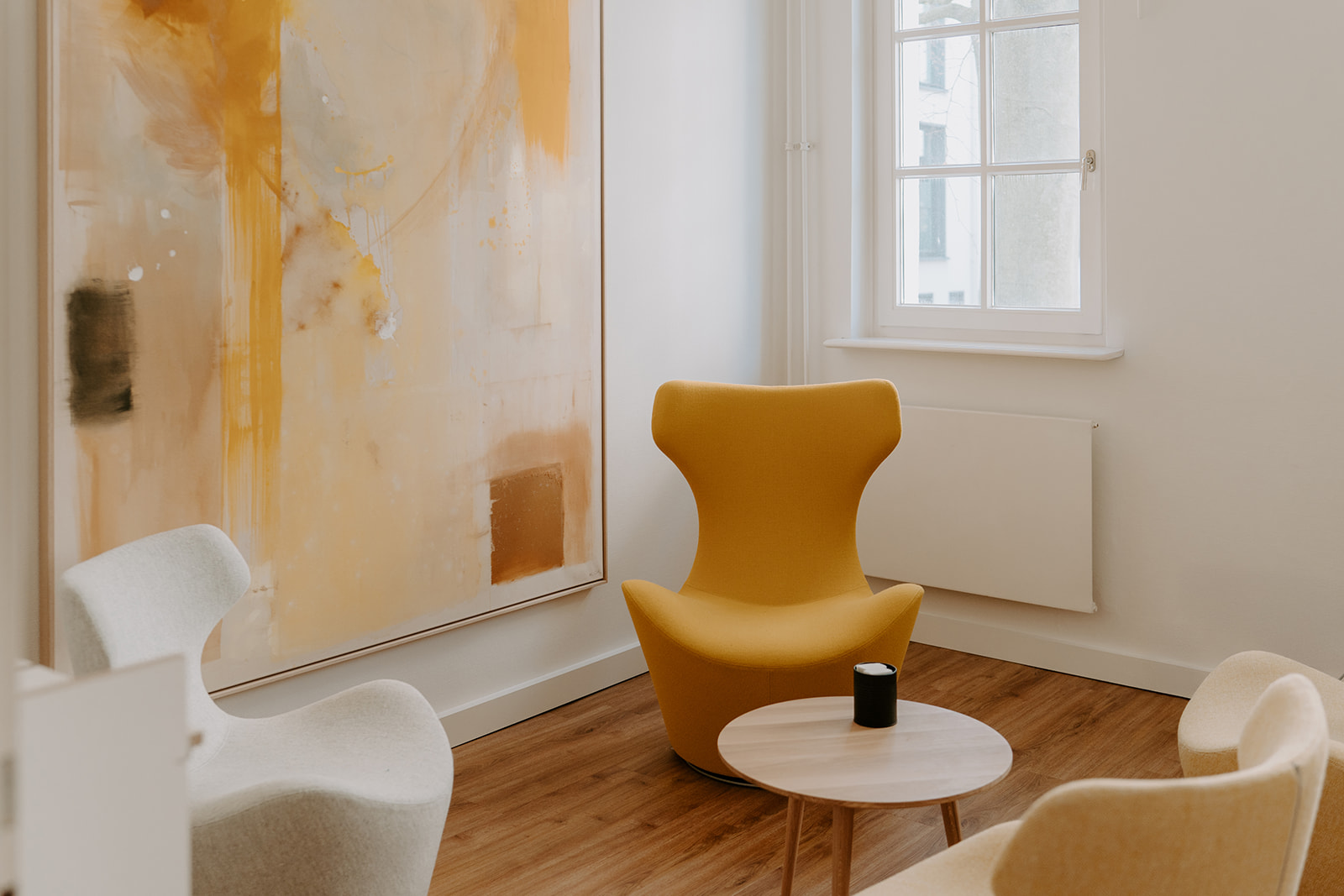 Ein heller Besprechungsraum mit zeitlosen Sitzmöbeln samt Couchtisch und einem offenen Sideboard im Hintergrund vor zwei Fenstern