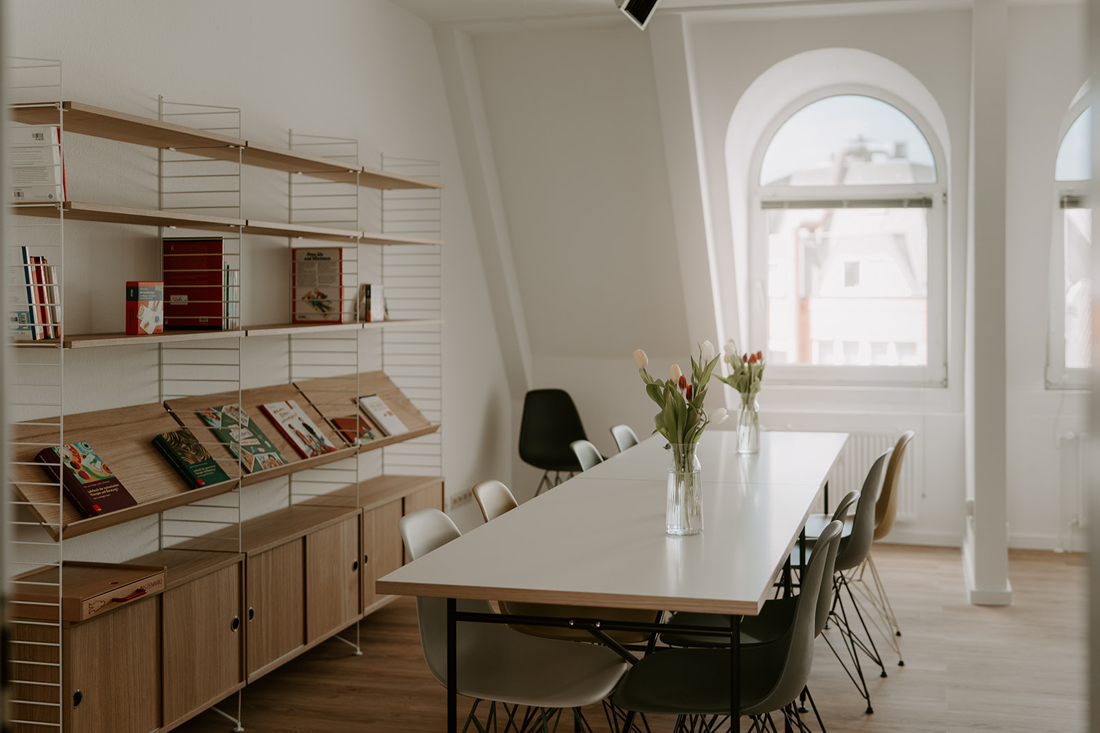 Ein heller Raum mit Rundbogenfenster und einem weißen Konferenztisch und Bücherregal