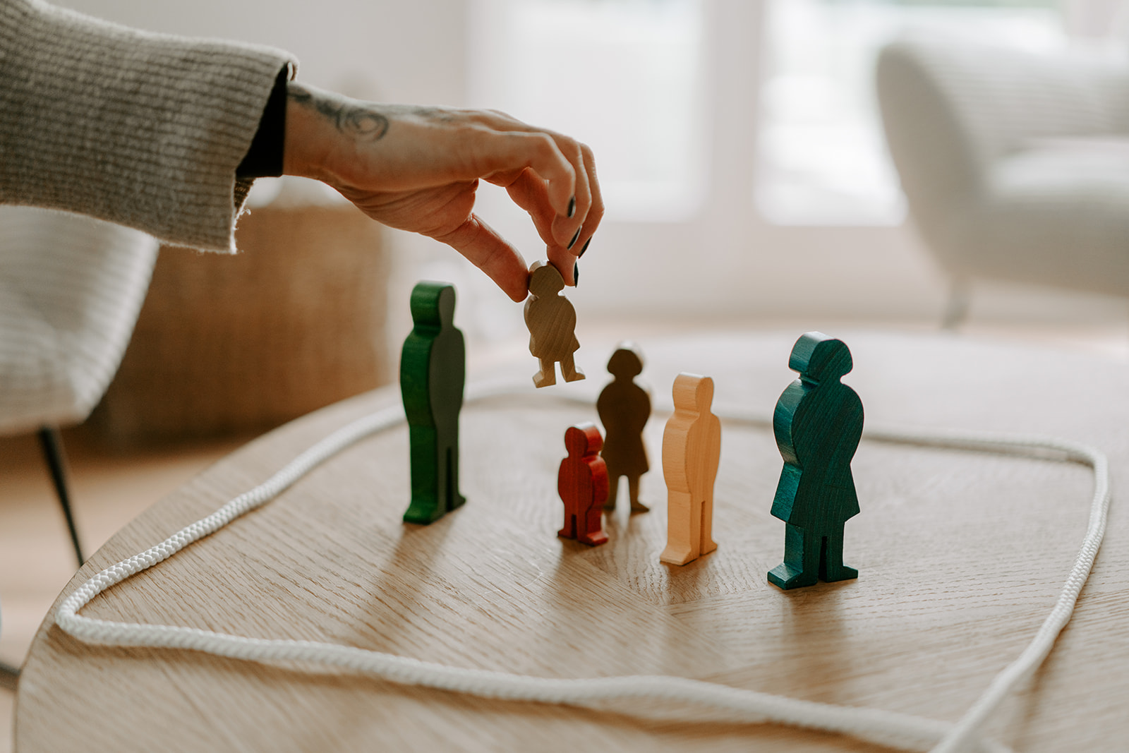 Eine Hand stellt Holzfiguren für eine Familienaufstellung auf einen Tisch