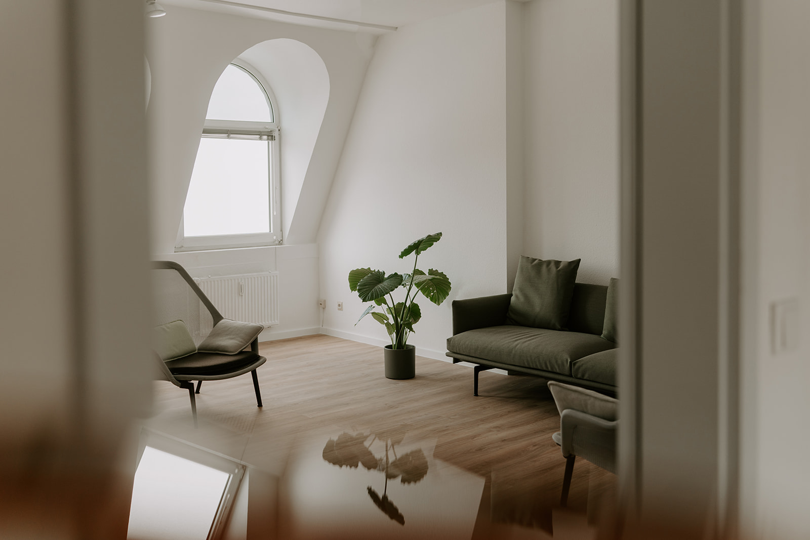 Ein schöner Raum mit Erker und Dielenboden im Hintergrund ein moosgrünes Sofa und ein hübscher Sessel