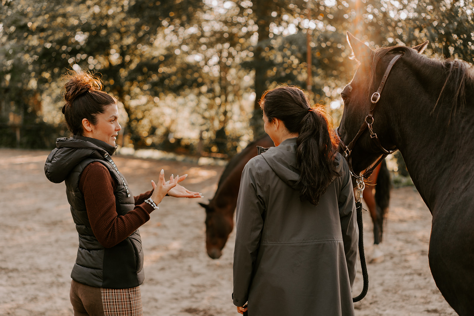 Auf einem Reitplatz stehen zwei Frauen mit einem Pferd: die eine Frau in Rückenansicht, Meltem Keklici im Profil